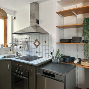 A modern kitchen with a stainless steel range hood, a built-in dishwasher, and a window above the sink.