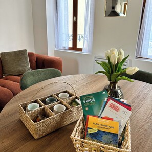 A room with a wooden table, a wicker basket with cups, a vase with white flowers, and a tourist map.