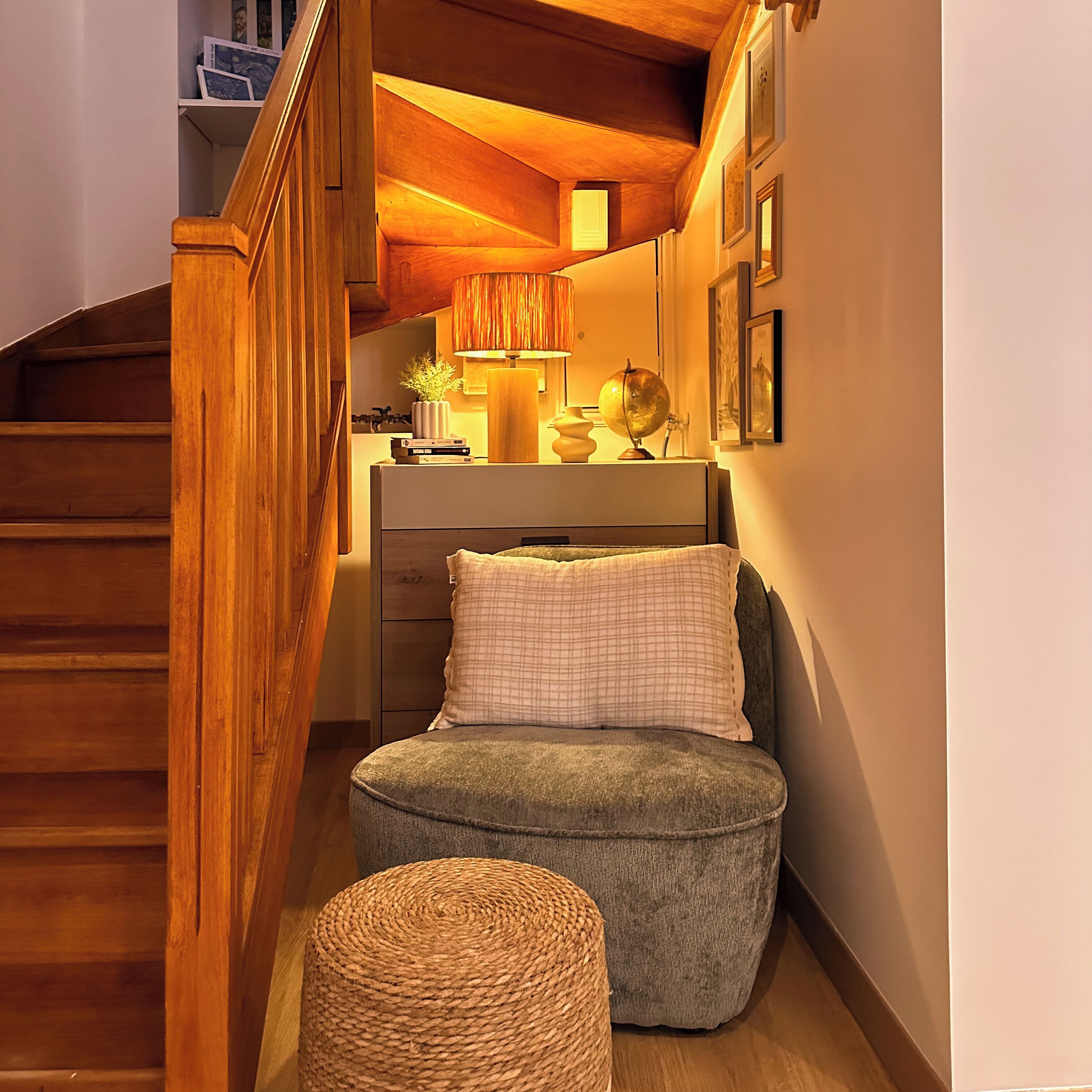 Ein gemütliches Zimmer mit einer Holztreppe, einem bequemen Sessel, einem kleinen Hocker und einem Schreibtisch mit Globus und Büchern.