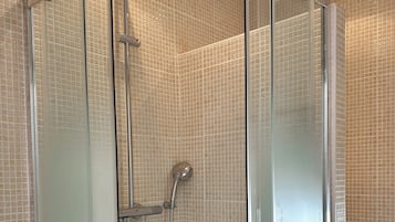 A walk-in glass shower with a handheld showerhead and a wall-mounted faucet.