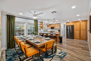 A modern kitchen with wooden cabinets, a stainless steel refrigerator, and a dining area with a large table and chairs.