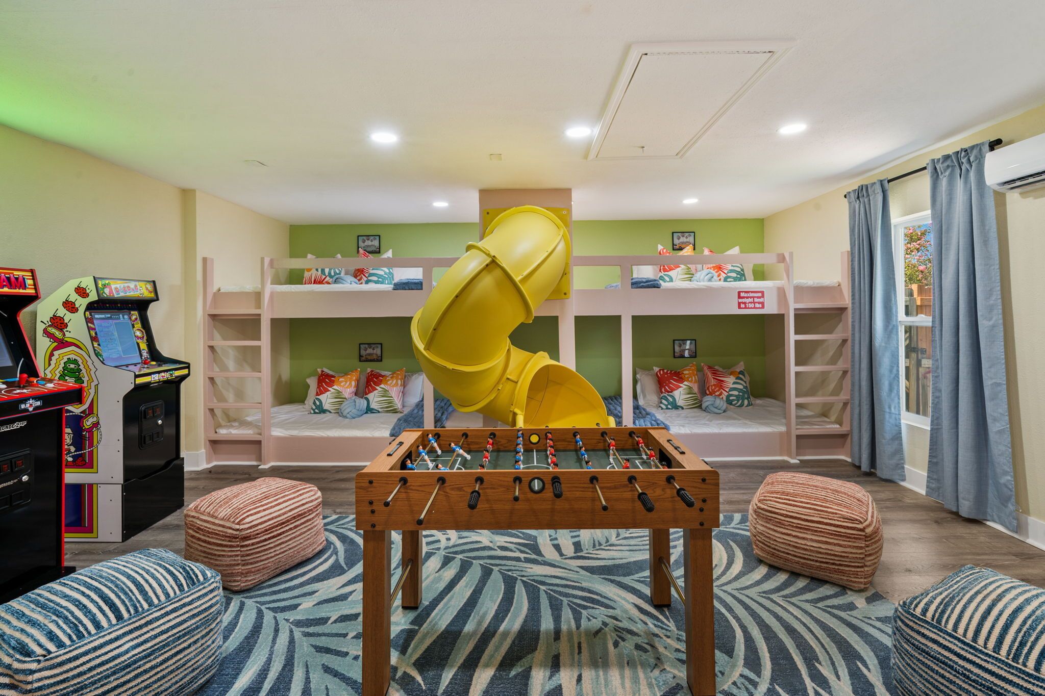 Zona de juegos infantiles con literas, mesa de fútbol de mesa y juegos de arcade.