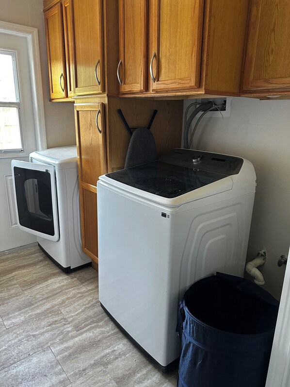 A compact kitchen with wooden cabinets, a washing machine, a dryer, and a trash bin.