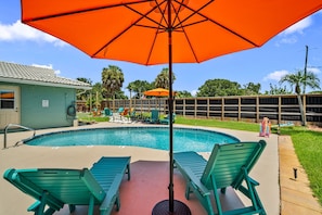 A swimming pool with lounge chairs and an umbrella.