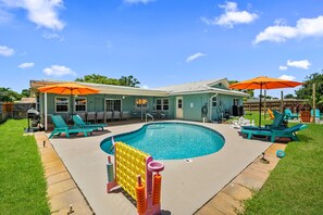 A backyard with a swimming pool, lounge chairs, and umbrellas.
