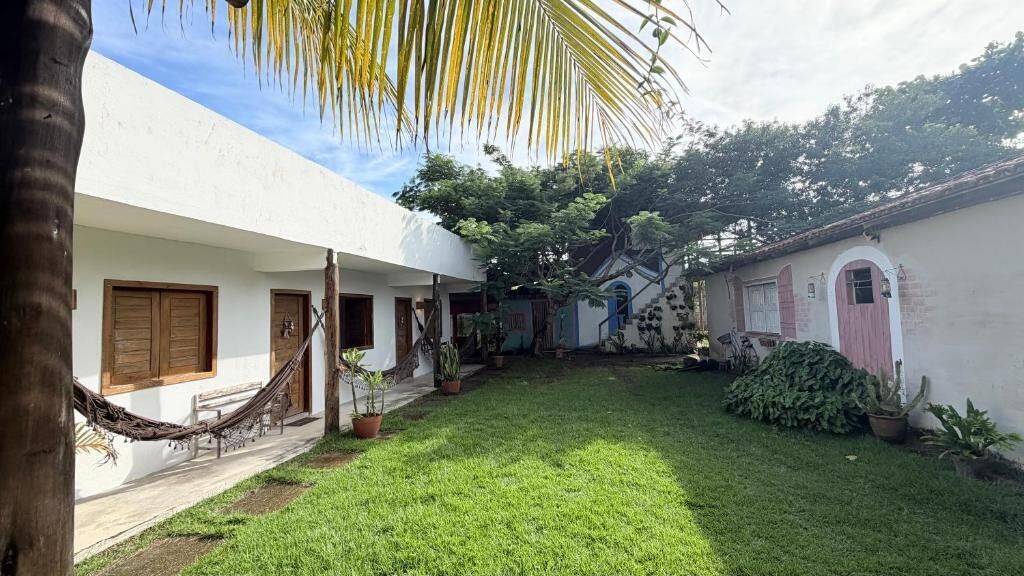 A courtyard with a hammock, potted plants, and a white building with wooden doors.