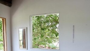 Una cama de madera con colcha y almohadas estampadas con motivos florales, una ventana con vistas a árboles y una pared blanca con un espejo y una pequeña señal.