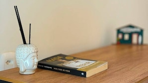 Uma mesa de madeira com um livro intitulado 'Nada Pode Me Ferir' de David Goggens e um vaso de cerâmica branca com alças pretas.