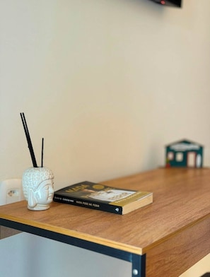 Una mesa de madera con un libro titulado 'Nada Pode Me Ferir' de David Goggins y un jarrón de cerámica blanca con detalles negros.
