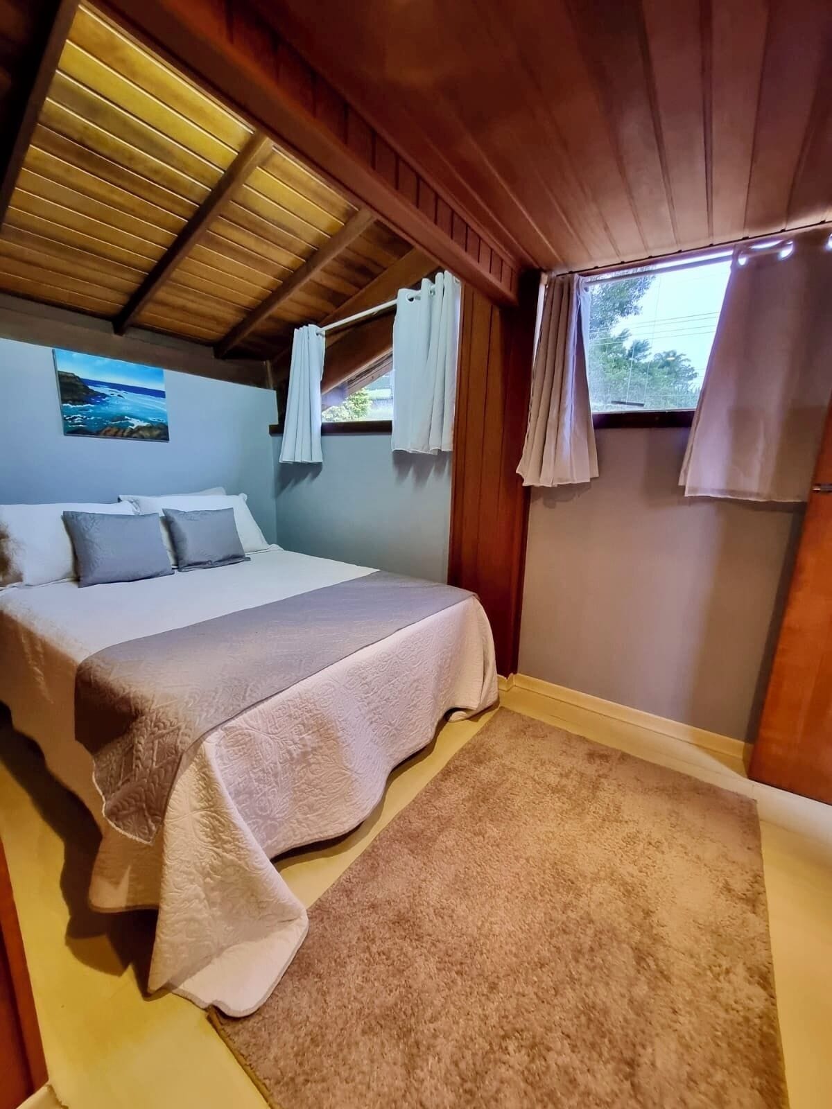 Quarto com cama, um quadro e janela com cortinas.