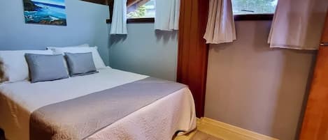 A bedroom with a bed, a painting, and a window with curtains.