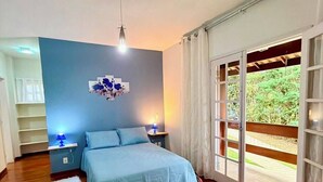 Un dormitorio con cama, mesitas de noche, cortinas en la ventana y vista a zonas verdes.