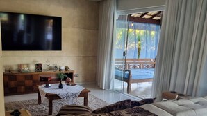 Una sala moderna con un televisor de pantalla plana grande, un sofá con un plaid estampado, una mesa de centro de madera y vistas a un balcón con mesa y sillas.