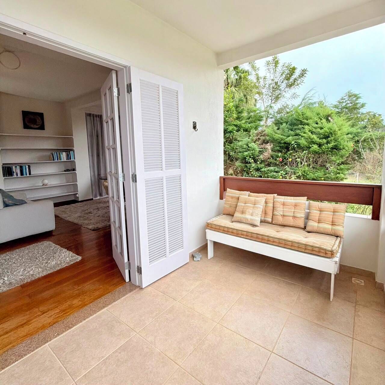 Um quarto com sofá branco, um banco de madeira, uma estante de livros e uma porta que dá para outro cômodo.