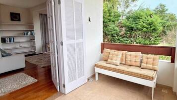 Um quarto com sofá branco, um banco de madeira, uma estante de livros e uma porta que dá para outro cômodo.