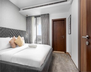 Una habitació d'hotel amb un llit, una porta de fusta i una finestra amb cortines.