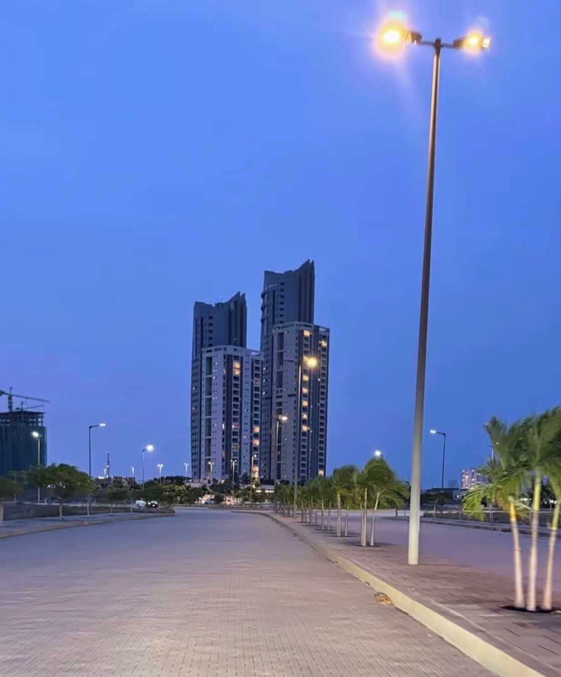 A paved walkway leading to high-rise buildings with multiple floors, street lamps, and a clear sky.