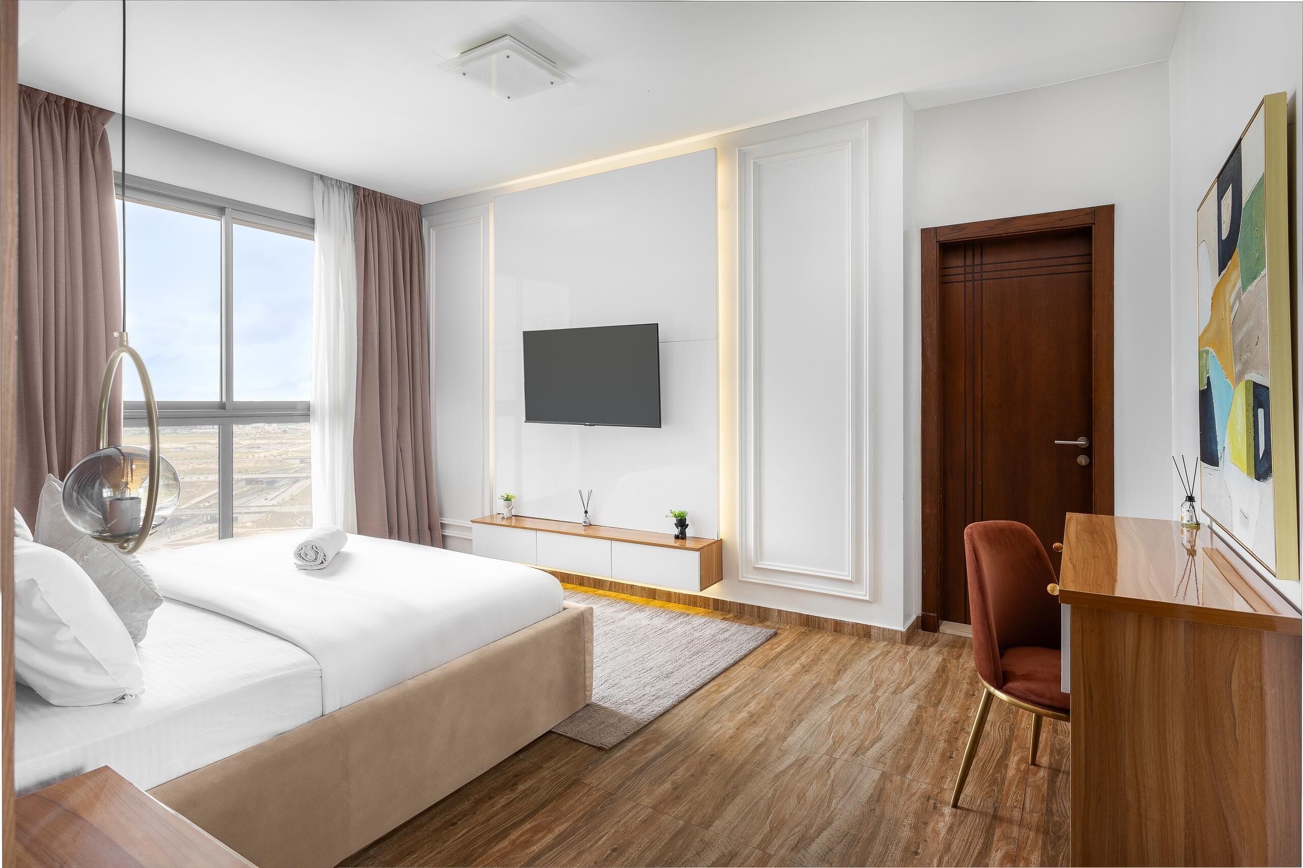 A hotel room with a bed, a desk, a chair, a TV, and a large window with curtains.