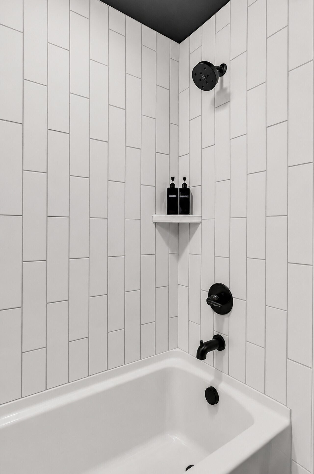 Een moderne badkamer met een wand betegeld in witte tegels, een witte badkuip en zwarte accessoires.