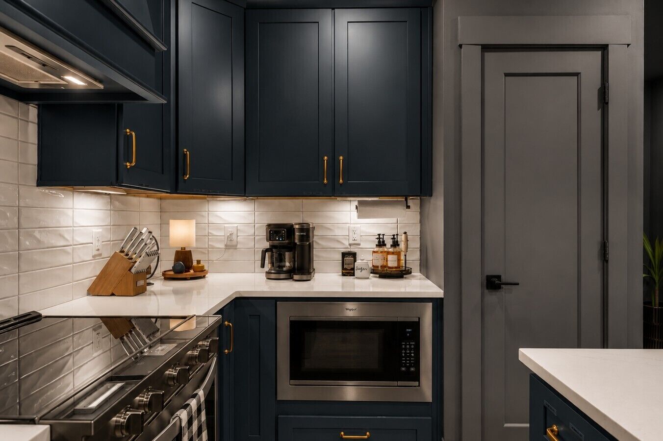 Une cuisine avec des meubles de couleur bleu foncé, une cuisinière en acier inoxydable, un four à micro-ondes et une machine à café.