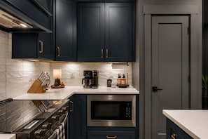 Een keuken met donkerblauwe kastjes, een roestvrijstalen fornuis, een magnetron en een koffiezetapparaat.