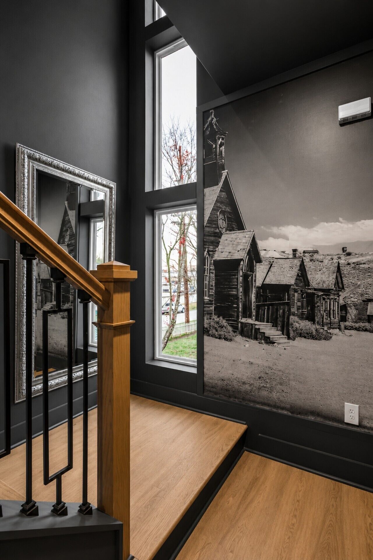 A staircase with a wooden handrail leading to a room with a large window overlooking a black and white mural of a rural scene.