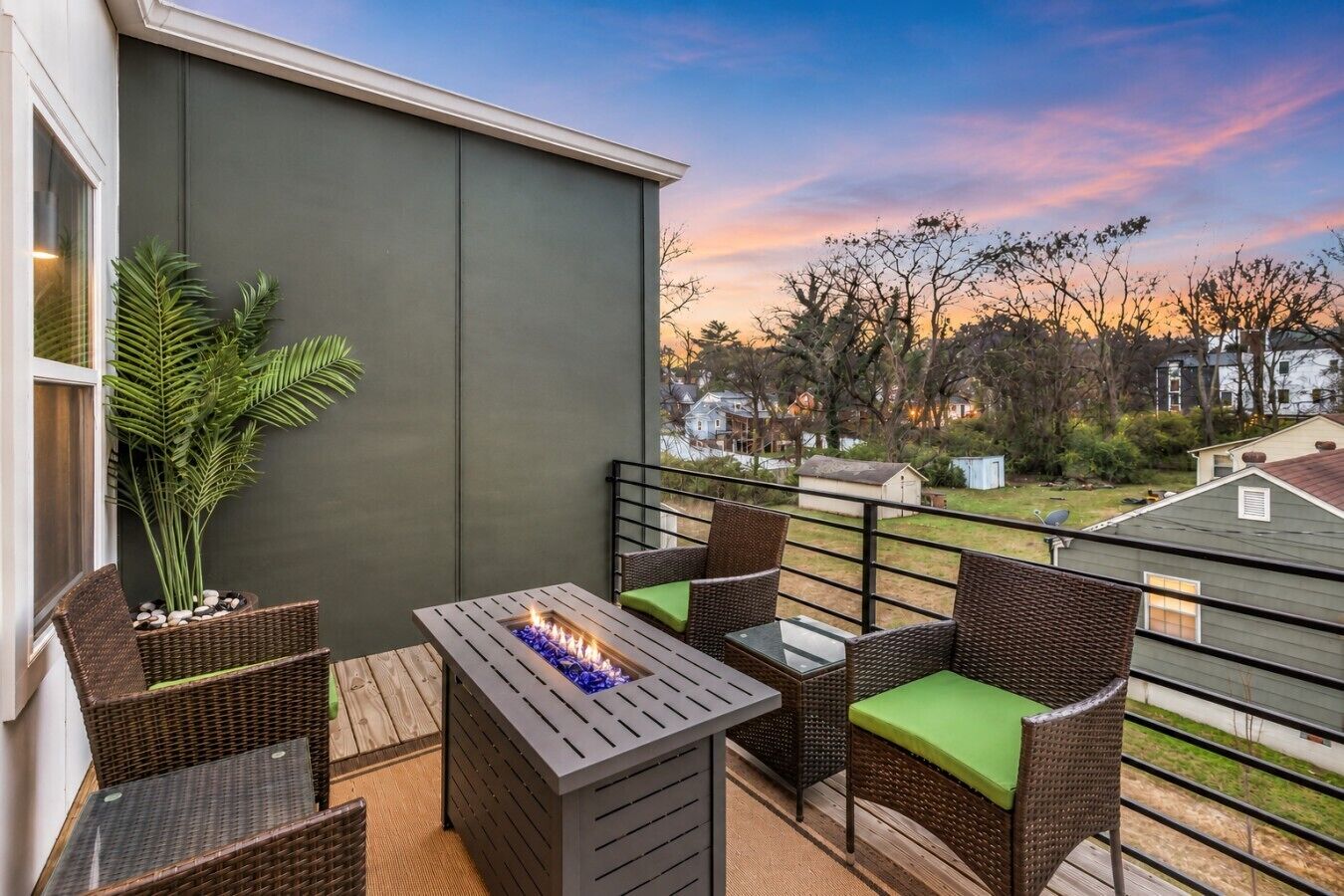 A balcony with outdoor furniture, a fire feature, and a view of the neighborhood during sunset.