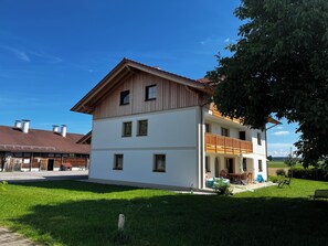 Ein zweistöckiges Gebäude mit einem Balkon, einer überdachten Veranda und einem gepflegten Rasen.