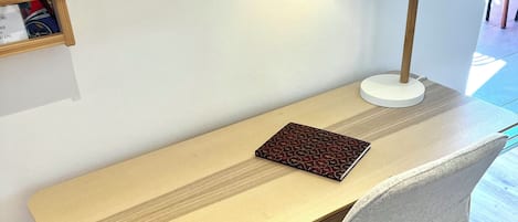 A wooden desk with a lamp, a chair, and a book on a shelf.