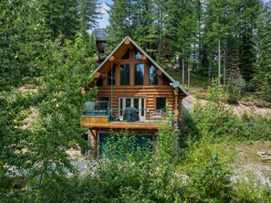 Une cabane en rondins dotée d’un balcon, entourée d’une forêt dense.