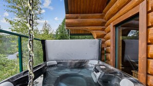 Un jacuzzi con panel de control, rodeado de paredes de cabaña de madera y barandilla de cristal.