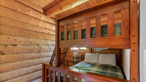Una cama litera con estructura de madera, una mesita con lámpara y un edredón a cuadros.