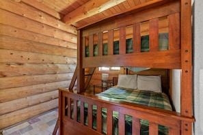 Ein Stockbett mit Holzrahmen, ein kleiner Tisch mit Lampe und eine karierte Bettdecke.