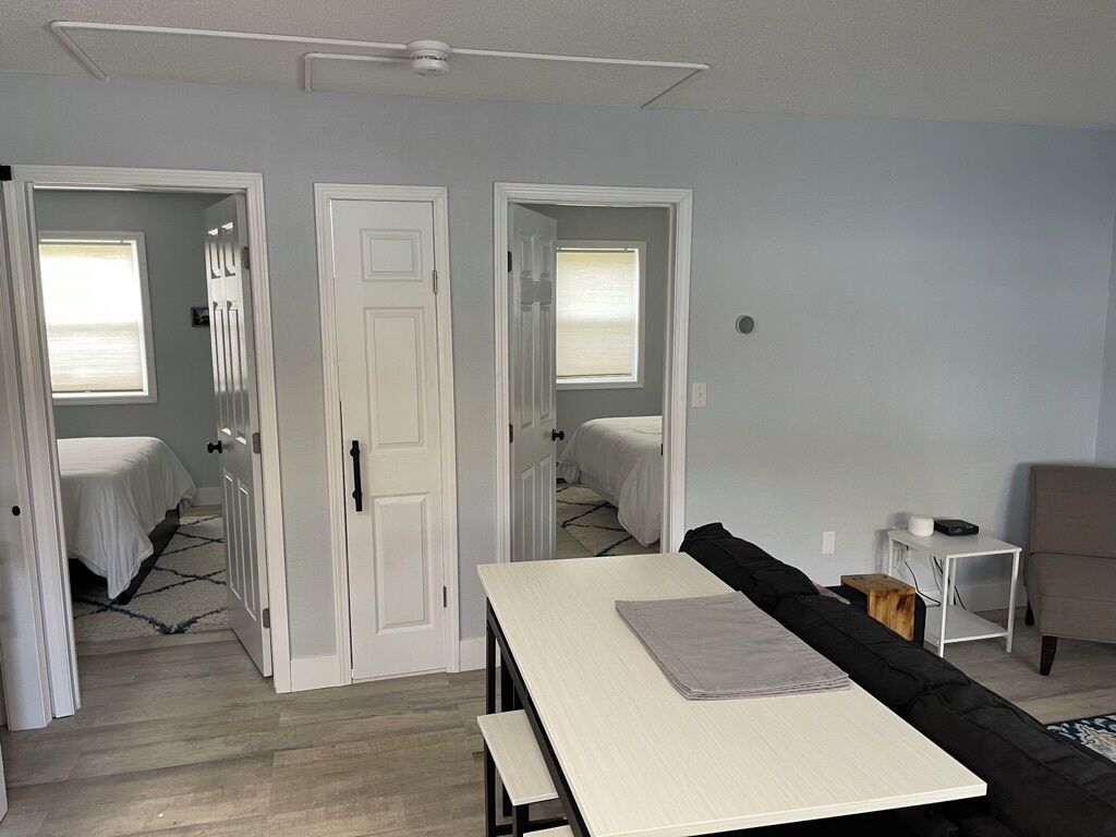 Ein Zimmer mit einem Bett, einem Tisch und einem Stuhl. Zwei Türen führen in andere Räume.