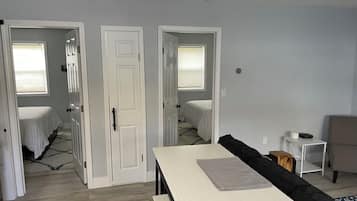 Ein Zimmer mit einem Bett, einem Tisch und einem Stuhl. Zwei Türen führen in andere Räume.