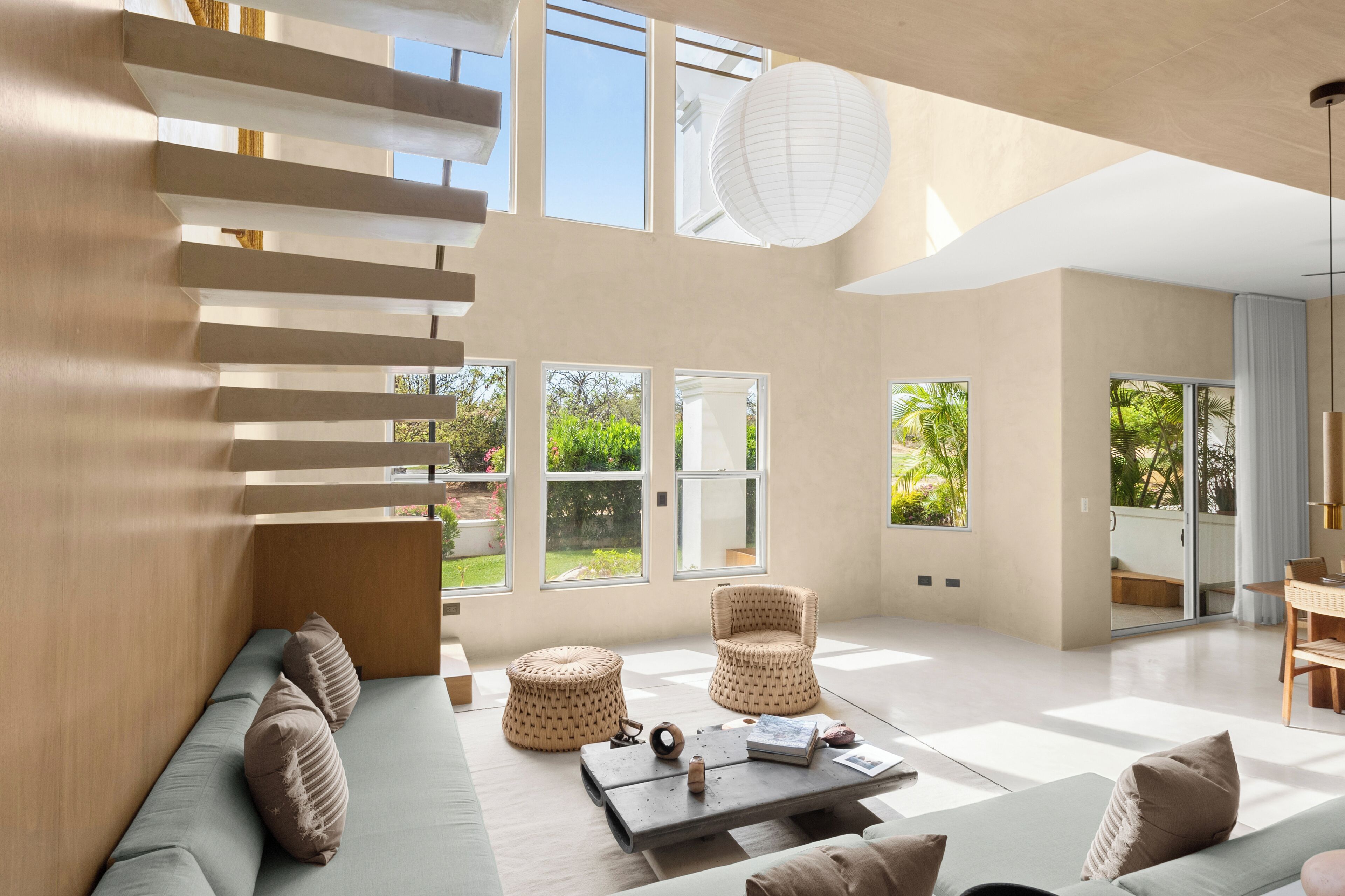 Un vaste espace de vie doté d’un haut plafond, de grandes fenêtres et d’un escalier moderne.
