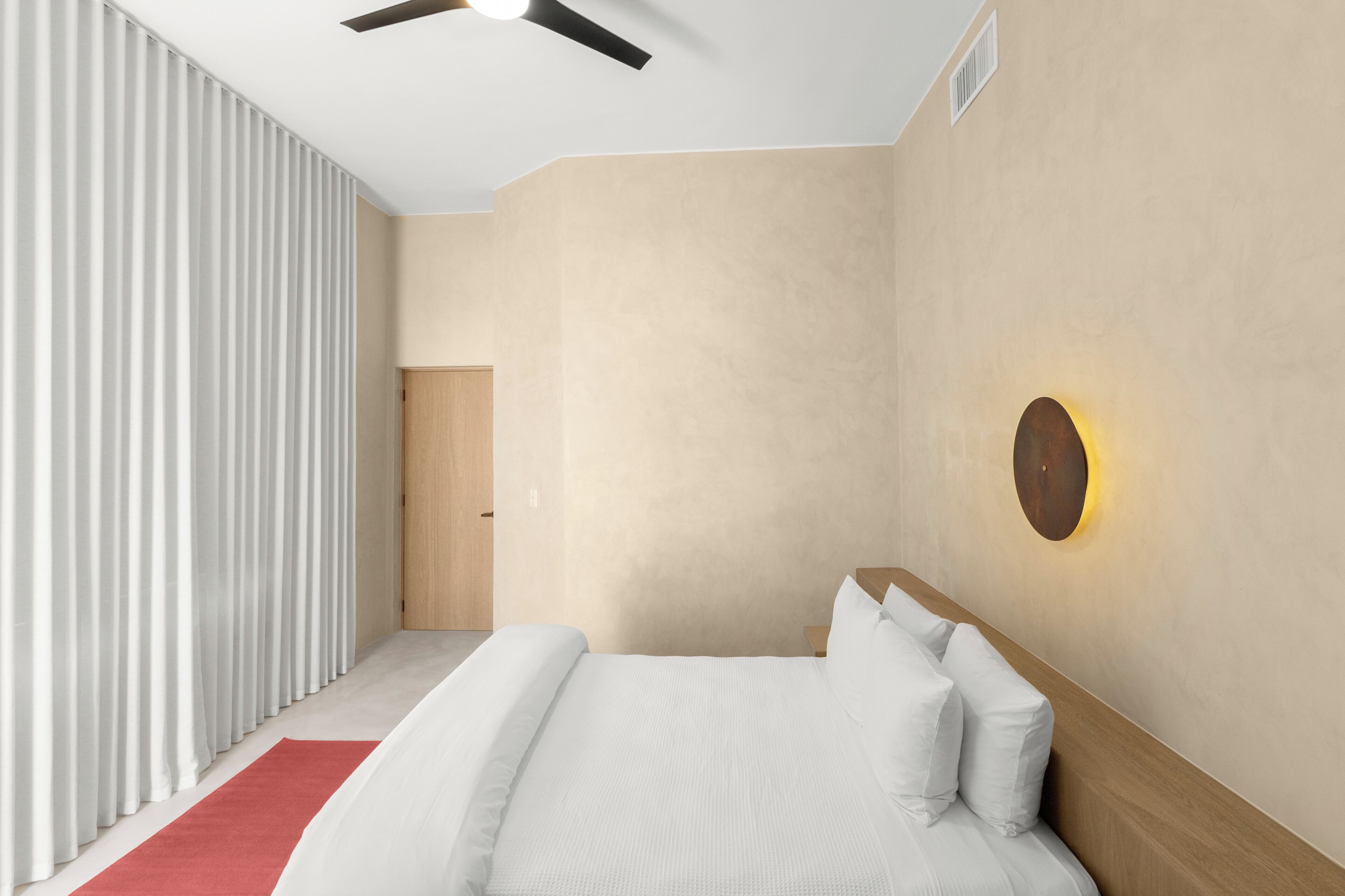A modern bedroom with a bed, a red rug, a ceiling fan, and a wall-mounted light fixture.