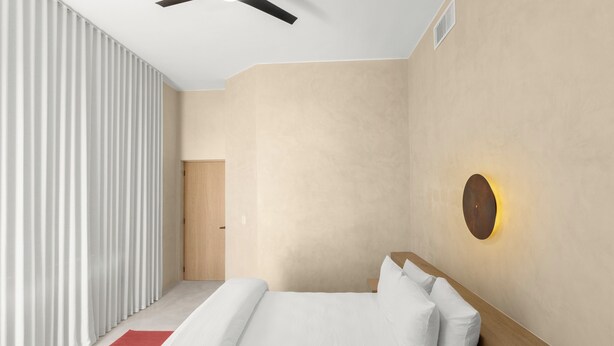 Quarto moderno com cama, tapete vermelho, ventilador de teto e luminária na parede.