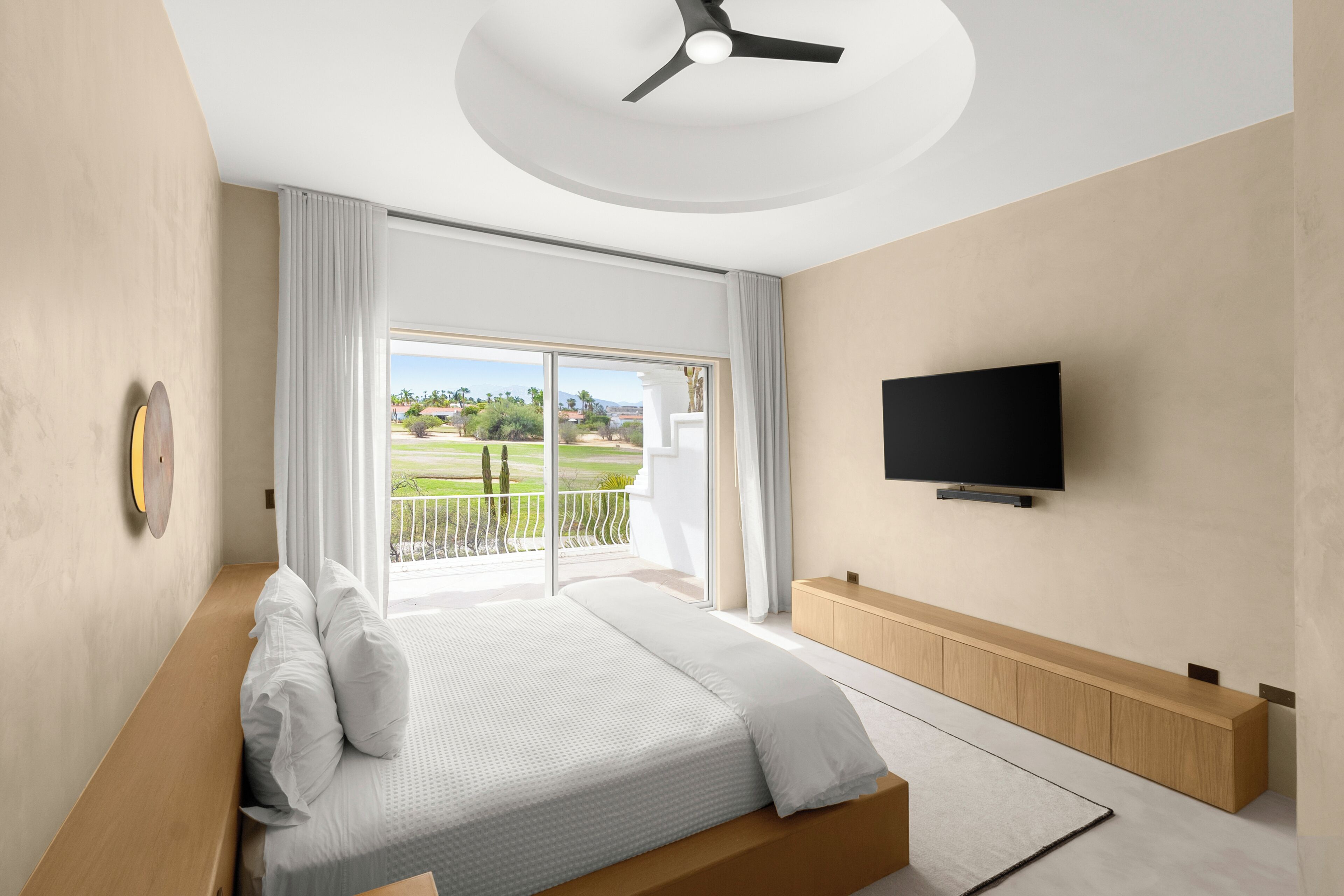Un dormitorio moderno con cama, televisor y balcón con vistas.