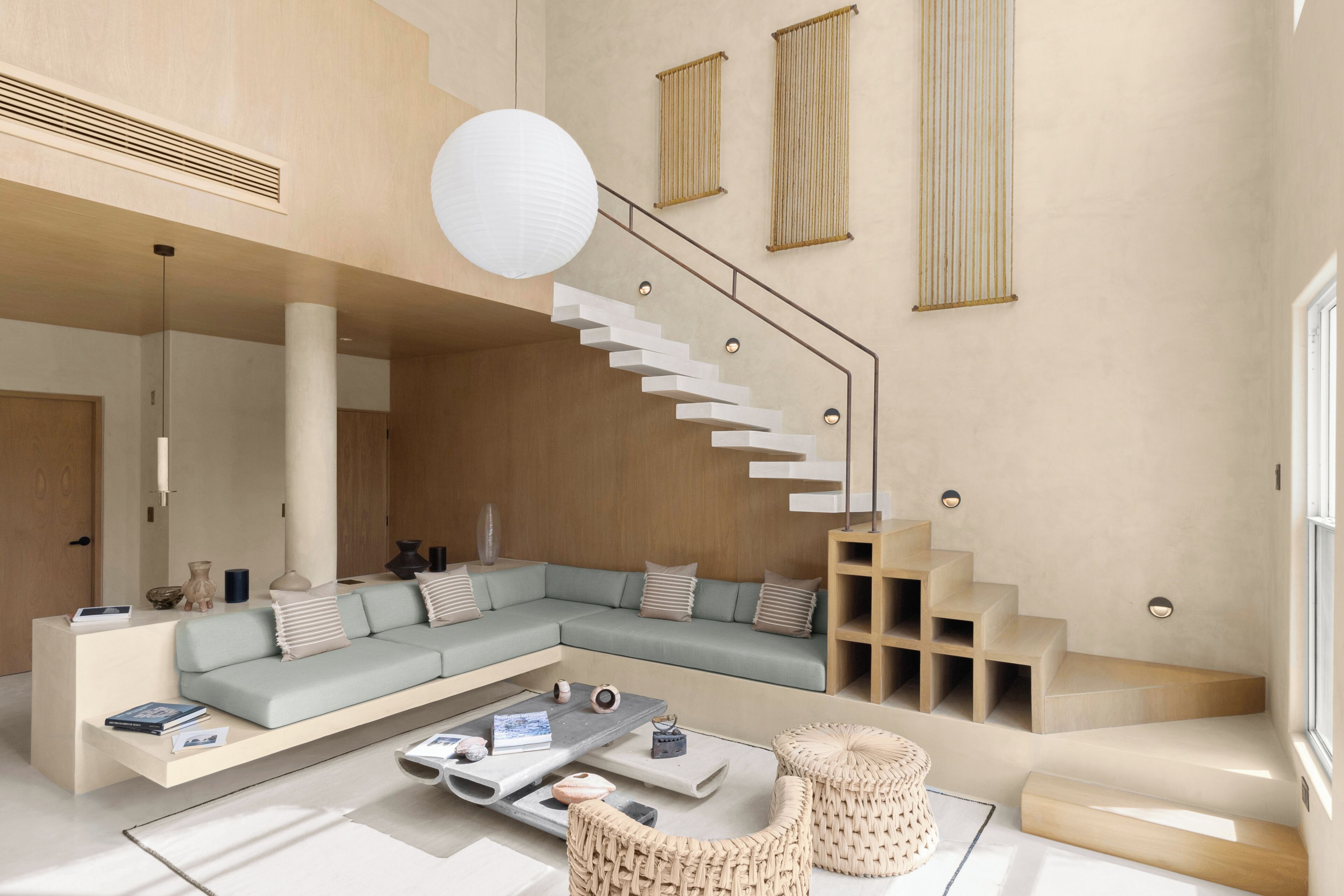 Un salon moderne avec un canapé d’angle, une table basse et un escalier au design original.