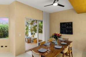 A dining area with a wooden table set for six, surrounded by wicker chairs, a vase with flowers, and a view of a garden through a glass door. - New listing  - Stylish Palmilla 3-Bedroom Condo with Shared Pool (Palmilla)