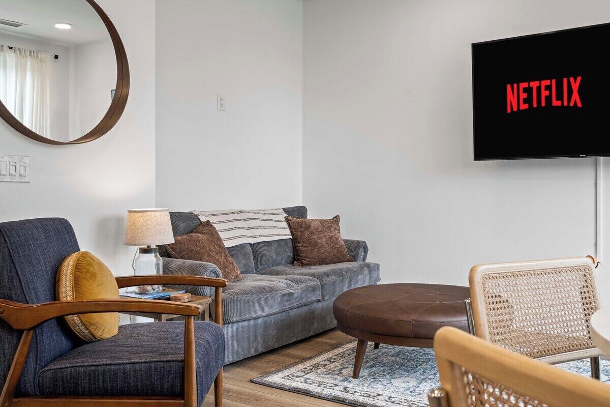 Un soggiorno con divano, poltrone, tavolino, una televisione con il logo Netflix e uno specchio rotondo appeso al muro.