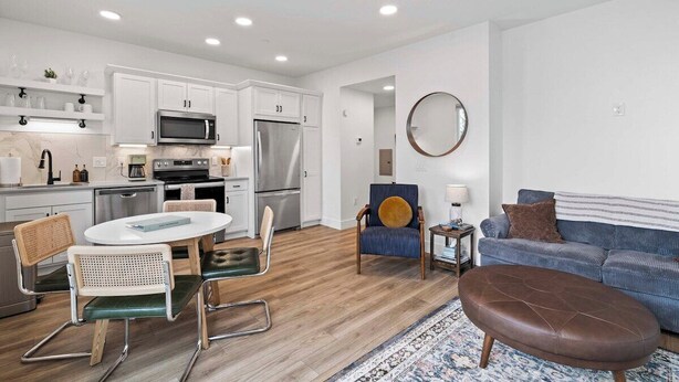 A modern kitchen with white cabinets, stainless steel appliances, and a dining area with a round table and chairs. - West Bay Views | Dog Friendly + Near Downtown TC (Traverse City)