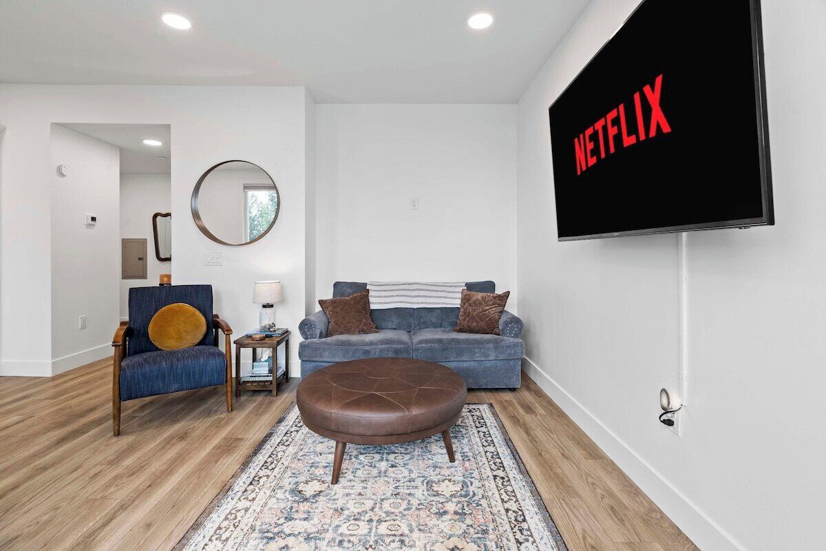Una sala de estar con un sofá, una mesa de centro, un televisor montado en la pared y un espejo.
