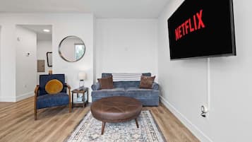 Una sala de estar con un sofá, una mesa de centro, un televisor montado en la pared y un espejo.