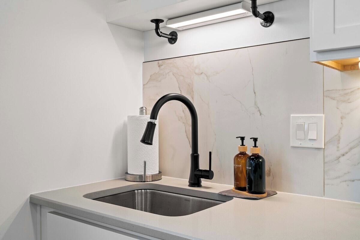 A modern kitchen with a stainless steel sink, black faucet, marble backsplash, and a light fixture above.