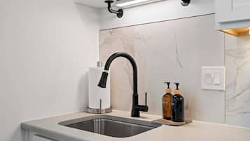Una cucina moderna con lavello in acciaio inossidabile, rubinetto nero, schienale in marmo e lampada a sospensione.