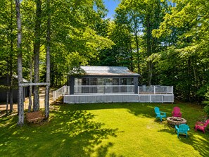 A cabin with a deck, surrounded by trees, and outdoor seating.