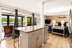 A modern kitchen with a granite countertop, grey cabinets, and a dining area with a blue sofa and two lamps.