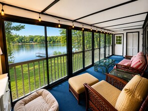 A spacious balcony with a view of a lake, furnished with a sofa, ottoman, and a glass table.